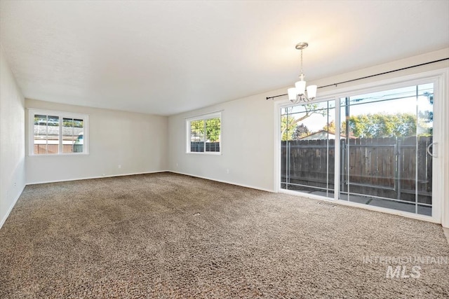 empty room featuring a chandelier, carpet flooring, and a wealth of natural light