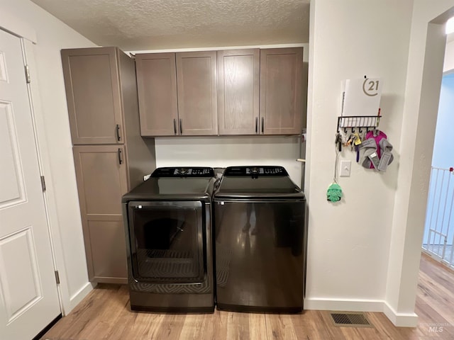 clothes washing area featuring cabinet space, light wood finished floors, visible vents, a textured ceiling, and washer and dryer