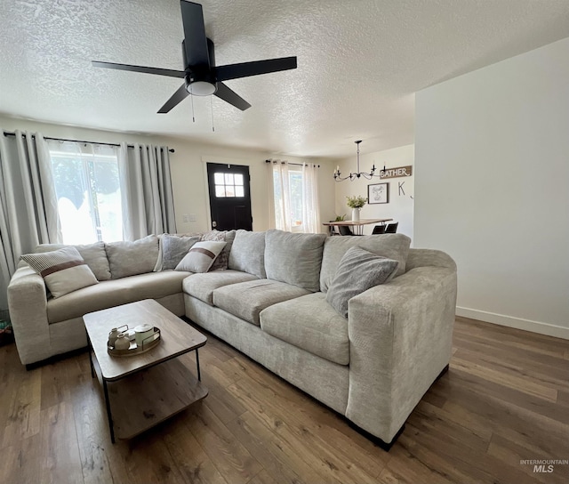 living area featuring a textured ceiling, dark wood-style flooring, ceiling fan with notable chandelier, and baseboards