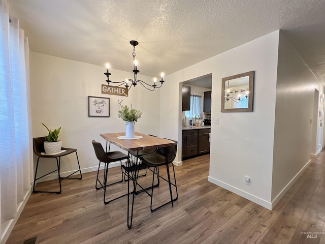 dining room featuring baseboards, visible vents, wood finished floors, a textured ceiling, and a notable chandelier