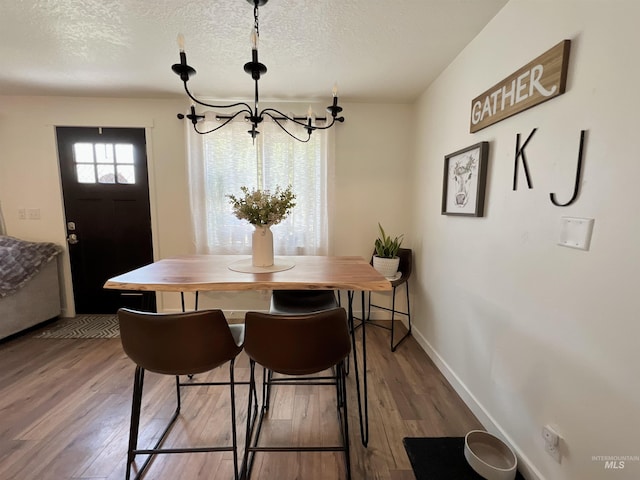 dining area with an inviting chandelier, a textured ceiling, baseboards, and hardwood / wood-style flooring