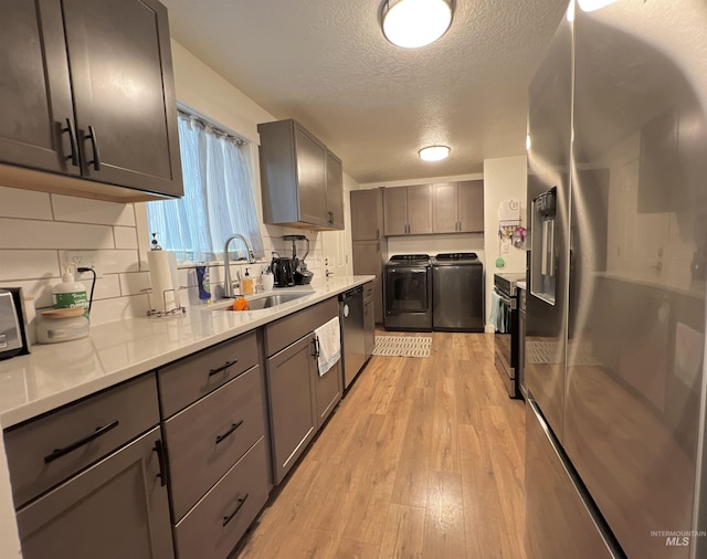 kitchen with light wood-style flooring, a sink, washer and dryer, appliances with stainless steel finishes, and gray cabinets