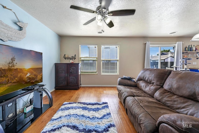 living room with a textured ceiling, ceiling fan, and light hardwood / wood-style flooring