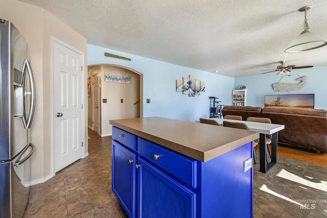 kitchen featuring stainless steel refrigerator with ice dispenser, a center island, ceiling fan, and blue cabinetry