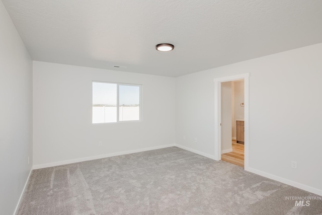 carpeted spare room with a textured ceiling and baseboards