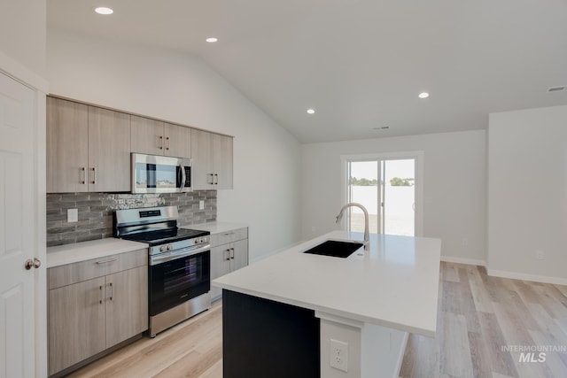 kitchen featuring light countertops, an island with sink, lofted ceiling, appliances with stainless steel finishes, and a sink