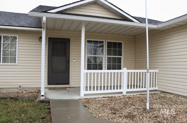 view of exterior entry featuring covered porch and a shingled roof