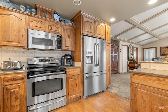 kitchen with vaulted ceiling, backsplash, appliances with stainless steel finishes, and light hardwood / wood-style flooring