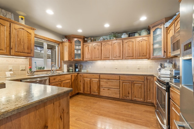 kitchen with appliances with stainless steel finishes, backsplash, light hardwood / wood-style floors, and sink