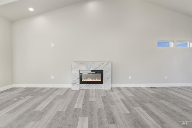 unfurnished living room featuring a fireplace, light hardwood / wood-style flooring, and lofted ceiling