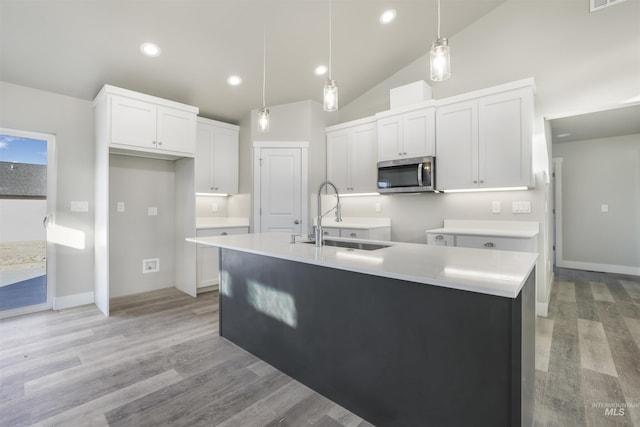 kitchen with decorative light fixtures, white cabinetry, an island with sink, sink, and light wood-type flooring