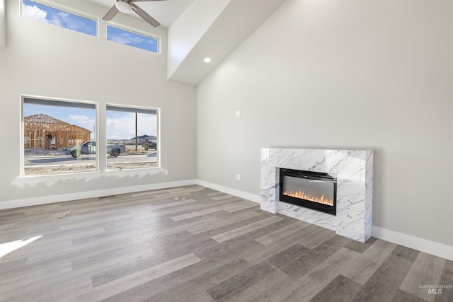 unfurnished living room featuring plenty of natural light, a high end fireplace, a towering ceiling, and light hardwood / wood-style flooring