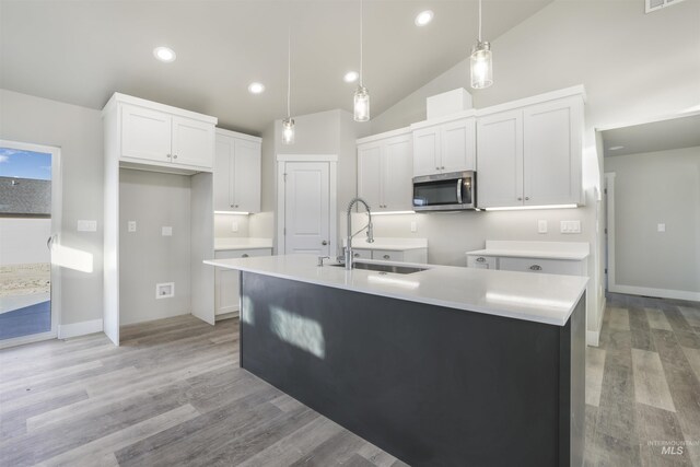 kitchen featuring pendant lighting, white cabinets, light hardwood / wood-style floors, sink, and a kitchen island with sink