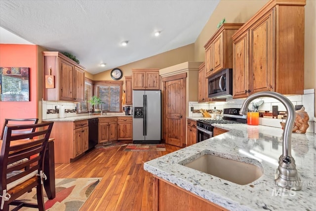 kitchen with lofted ceiling, sink, appliances with stainless steel finishes, light stone countertops, and light wood-type flooring