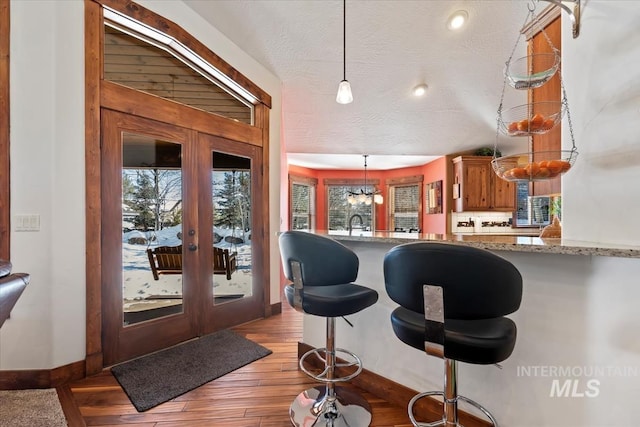 interior space with light hardwood / wood-style floors, plenty of natural light, light stone counters, and decorative light fixtures