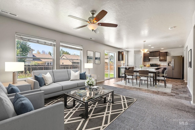 carpeted living room with a textured ceiling, plenty of natural light, and ceiling fan