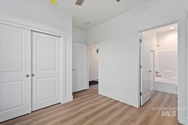 unfurnished bedroom with connected bathroom, light hardwood / wood-style flooring, a closet, and ceiling fan