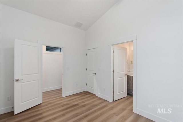 unfurnished bedroom with lofted ceiling, ensuite bath, and light hardwood / wood-style flooring