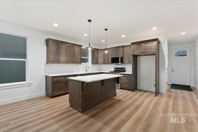 kitchen with a center island, hanging light fixtures, light hardwood / wood-style flooring, appliances with stainless steel finishes, and decorative backsplash