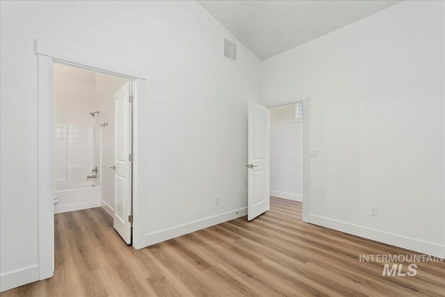 unfurnished bedroom featuring connected bathroom, vaulted ceiling, and light hardwood / wood-style floors