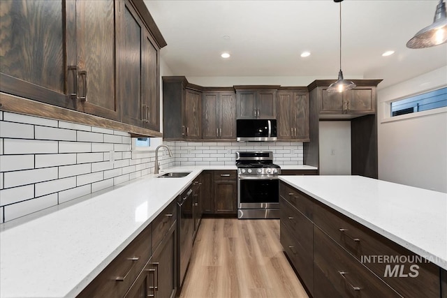 kitchen featuring appliances with stainless steel finishes, tasteful backsplash, sink, hanging light fixtures, and light hardwood / wood-style floors