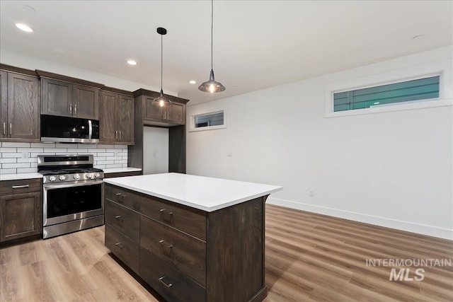 kitchen featuring appliances with stainless steel finishes, backsplash, a center island, light hardwood / wood-style floors, and decorative light fixtures