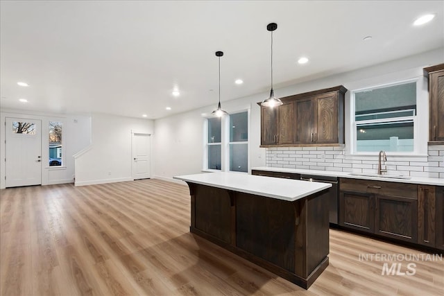 kitchen featuring a breakfast bar, sink, decorative light fixtures, a center island, and light hardwood / wood-style flooring