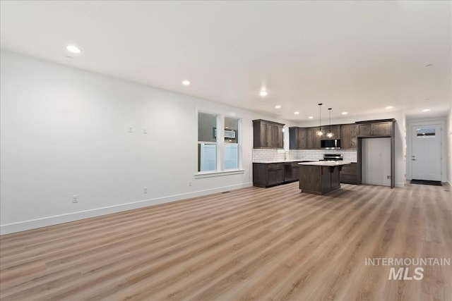 kitchen featuring pendant lighting, light hardwood / wood-style flooring, appliances with stainless steel finishes, a center island, and decorative backsplash