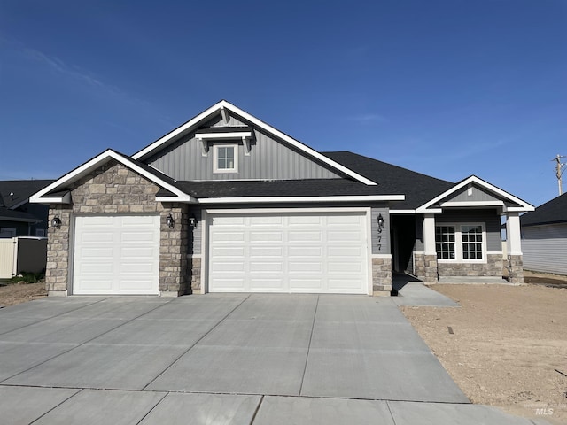 craftsman-style home featuring board and batten siding, driveway, an attached garage, a shingled roof, and stone siding