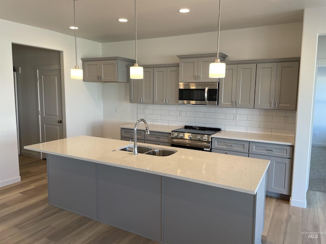 kitchen with appliances with stainless steel finishes, a sink, wood finished floors, backsplash, and gray cabinetry