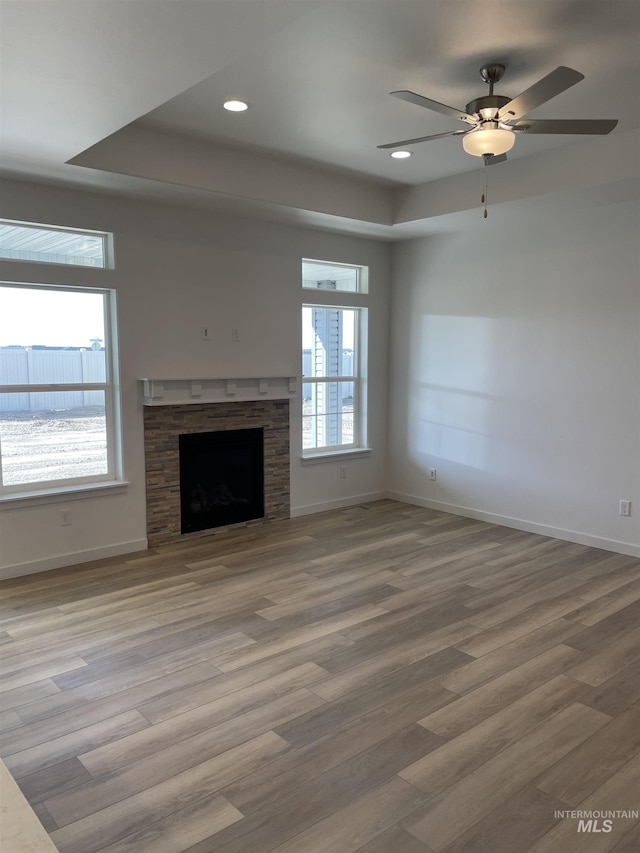 unfurnished living room featuring baseboards, a stone fireplace, wood finished floors, and a wealth of natural light