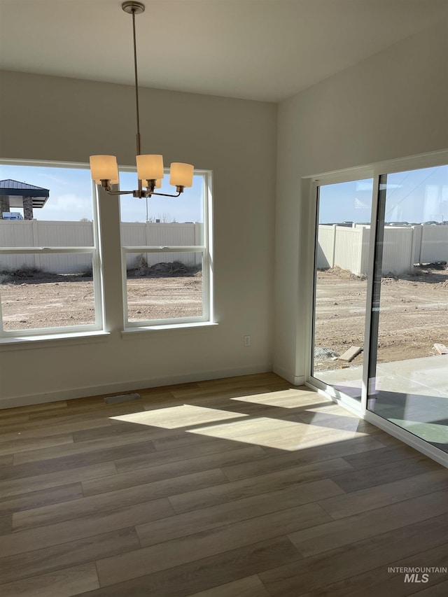 unfurnished dining area with an inviting chandelier and wood finished floors