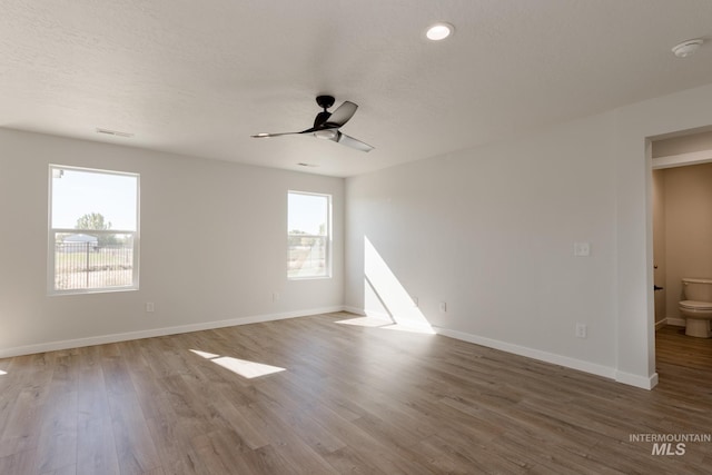 empty room with a textured ceiling, wood finished floors, a ceiling fan, and baseboards