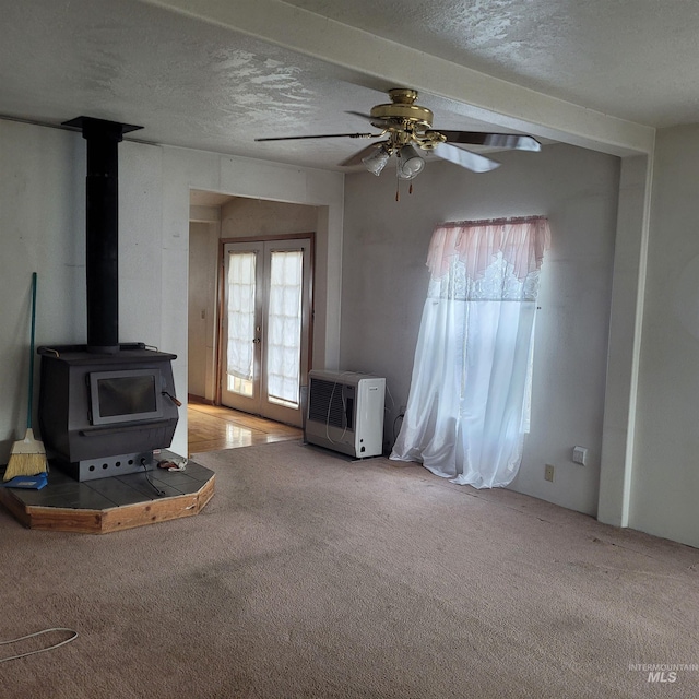 unfurnished living room featuring heating unit, a wood stove, french doors, a textured ceiling, and carpet flooring