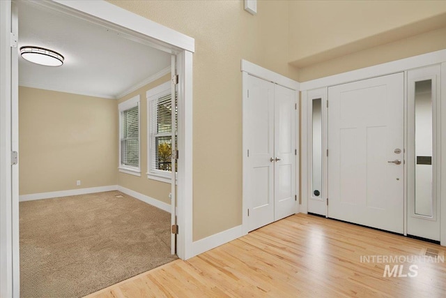 carpeted foyer with crown molding, wood finished floors, and baseboards