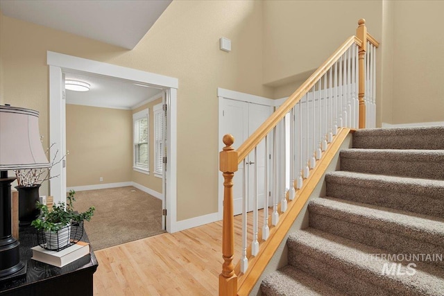 staircase with a high ceiling, crown molding, wood finished floors, and baseboards