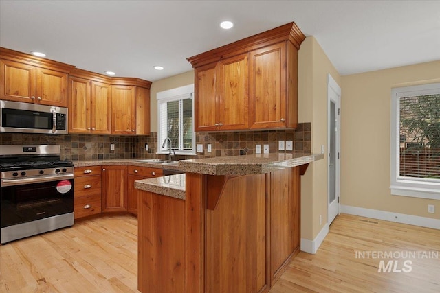 kitchen with tasteful backsplash, a sink, appliances with stainless steel finishes, a peninsula, and brown cabinets