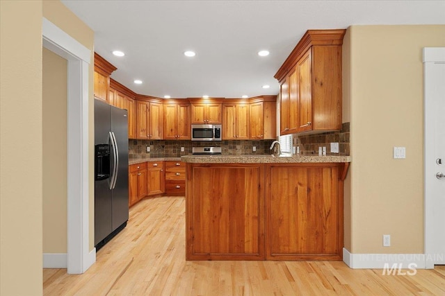 kitchen with tasteful backsplash, light wood-type flooring, a peninsula, and stainless steel appliances