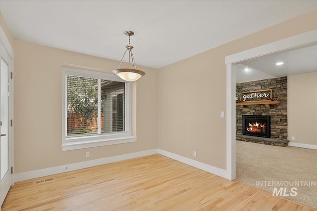 unfurnished dining area featuring visible vents, baseboards, wood finished floors, and a fireplace