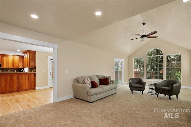 living area with light carpet, vaulted ceiling, a ceiling fan, and a textured ceiling