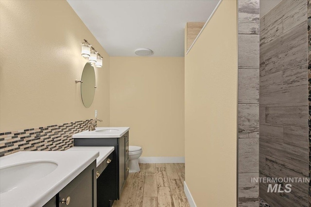 full bath with two vanities, toilet, wood finished floors, a sink, and decorative backsplash