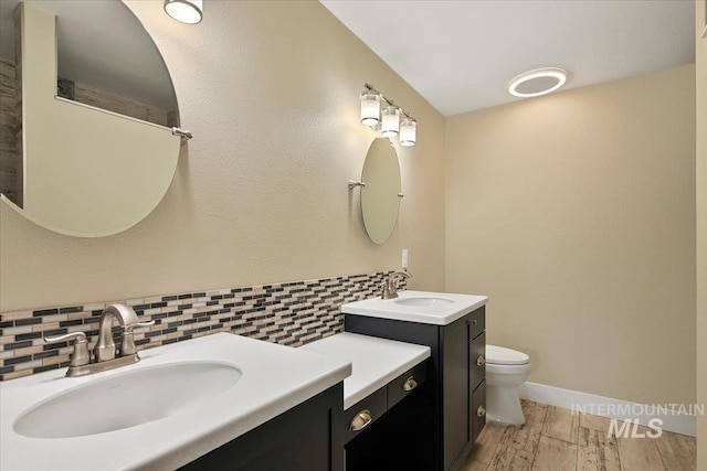 bathroom featuring toilet, wood finished floors, a sink, and backsplash