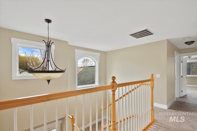 hallway featuring visible vents, baseboards, an upstairs landing, and carpet floors
