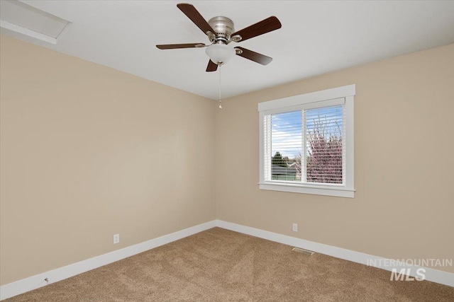 carpeted spare room featuring visible vents, baseboards, a ceiling fan, and attic access