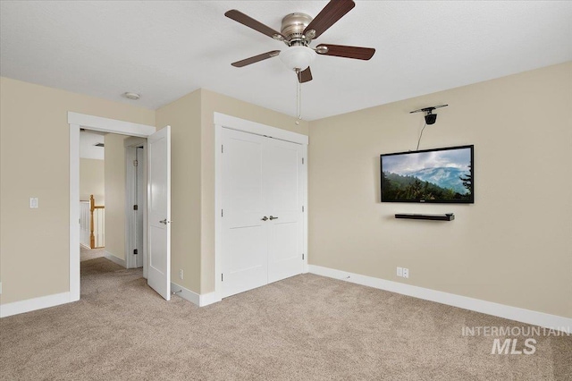unfurnished bedroom featuring a closet, light colored carpet, baseboards, and a ceiling fan