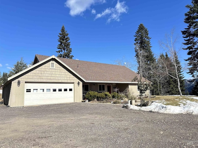 view of front of house featuring an attached garage, gravel driveway, and roof with shingles