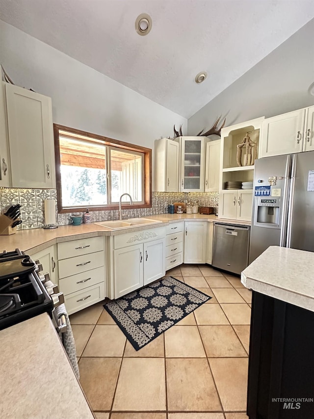 kitchen with a sink, tasteful backsplash, stainless steel appliances, light tile patterned floors, and vaulted ceiling