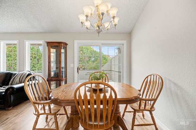 dining area featuring light hardwood / wood-style floors, a healthy amount of sunlight, a textured ceiling, and a chandelier