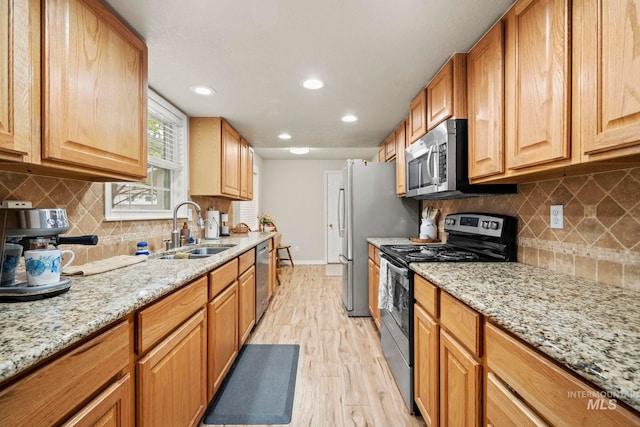 kitchen featuring light stone countertops, appliances with stainless steel finishes, sink, and light wood-type flooring