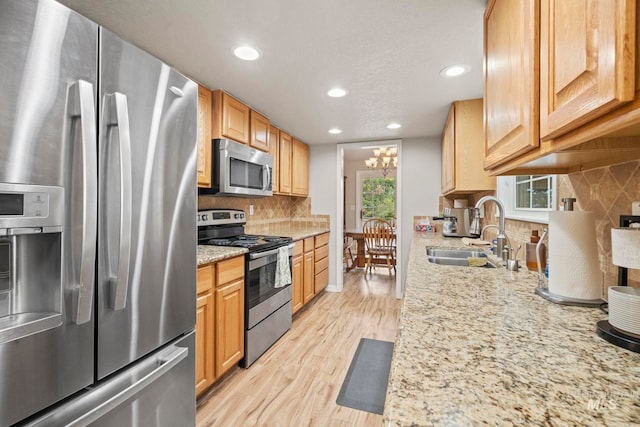 kitchen with tasteful backsplash, appliances with stainless steel finishes, sink, light wood-type flooring, and light stone counters